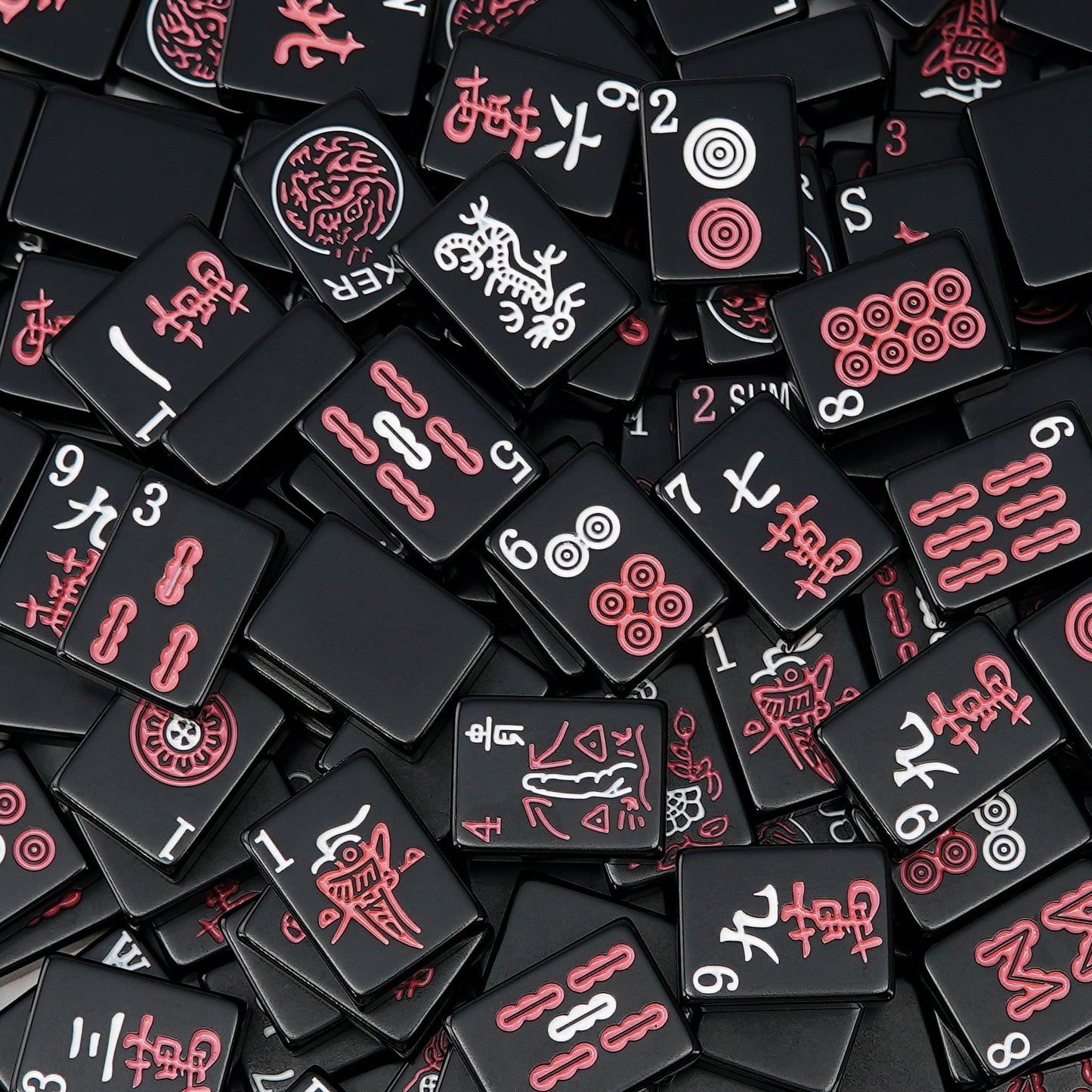 black mahjong tiles scattered closely together showing red and white symbols on a dark surface